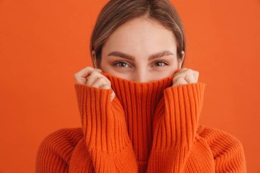 Süveter içinde saklanan genç, tatlı bir kız izole edilmiş turuncu arka planda.