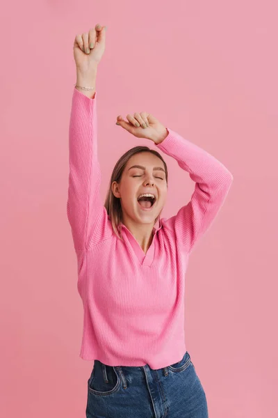 Young happy girl in pink blouse dancing with closed eyes and opened mouth over isolated pink background
