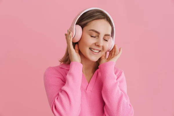 stock image Young beutiful smiling girl enjoying music with closed eyes in pink headphones over isolated pink background