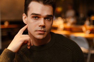 Süveter giyen, düşünen ve kafede kameraya bakan genç, beyaz esmer adam.