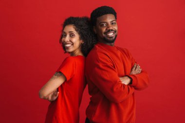 Siyah mutlu adam ve kadın gülümsüyor ve kırmızı arka planda izole edilmiş kameraya bakıyor.