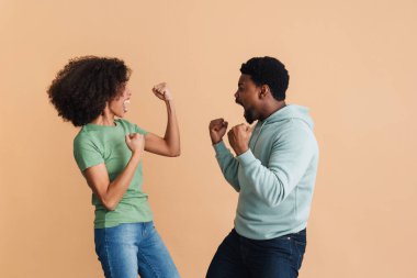 Siyahi adam ve kadın, bej arka planda izole edilmiş kazananlar gibi gülüp el kol sallıyor.