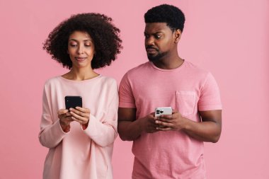 Siyahi, ciddi bir adam pembe arka planda tek başına kadının cep telefonuna bakıyor.