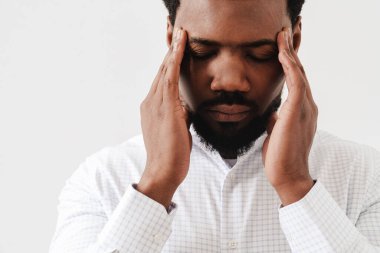 Siyah, yorgun, başı ağrıyan, şakaklarını ovalayan, beyaz arka planda soyutlanmış bir adam.