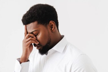 Siyah, yorgun bir adam beyaz arka planda yüzünü kapatırken poz veriyor.