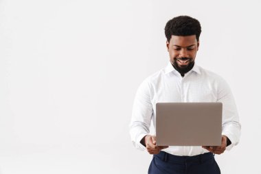 Siyah sakallı adam dizüstü bilgisayar kullanıyor ve beyaz arka planda sırıtıyor.