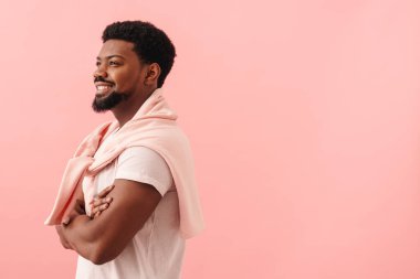 Siyah bir adam tişört giyip gülümsüyor ve pembe arka planda soyutlanmış bir şekilde yan tarafa bakıyor.