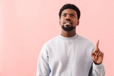 Siyah, sakallı, parmağıyla yukarıya bakan, pembe arka planda soyutlanmış bir adam.