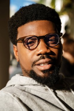 Siyah sakallı adam, kafeteryada otururken kameraya bakıyor.