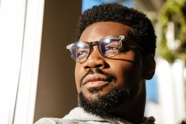 Gözlüklü siyah sakallı adam kafeteryada otururken yan bakıyor.