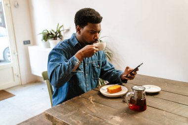 Kafede çay içerken cep telefonu kullanan siyah sakallı bir adam.