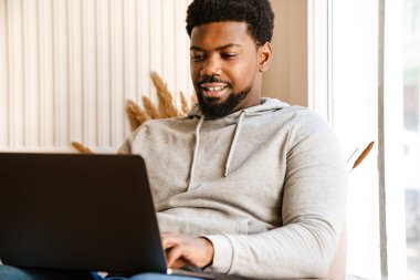 Siyah sakallı bir adam kafede otururken dizüstü bilgisayarla çalışıyor.