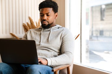 Siyah sakallı bir adam kafede otururken dizüstü bilgisayarla çalışıyor.