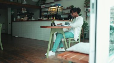 Kafede kulaklıkla dizüstü bilgisayarda çalışan Afrikalı şirin bir adamın yan görüntüsü.