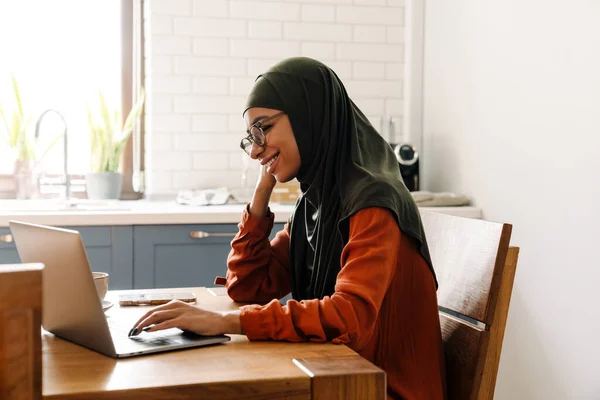 Młoda Piękna Uśmiechnięta Kobieta Hidżabie Okulary Pracujące Laptopem Przytulnej Kuchni — Zdjęcie stockowe
