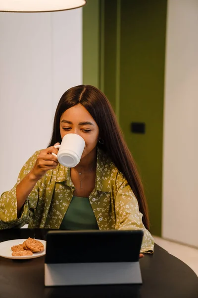 Młoda Piękna Długowłosa Kobieta Pijąca Kawę Ciasteczkami Patrząca Tablet Domu — Zdjęcie stockowe
