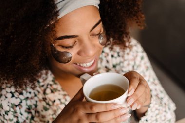Gözleri kapalı çay içen güzel, gülümseyen Afrikalı bir kadının portresi.