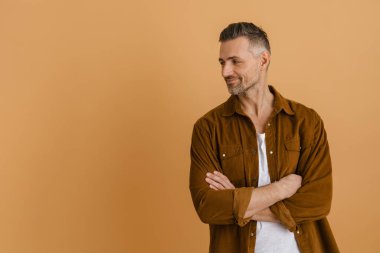 Beyaz gri tişörtlü adam gülümsüyor ve bej arka planda tek başına bir kenara bakıyor.