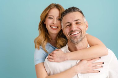 Beyaz mutlu çift sarılıyor ve mavi arka planda izole edilmiş kameraya bakıyor.