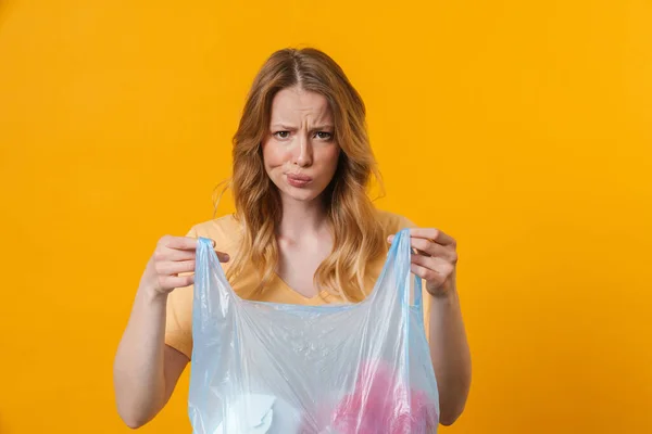 若いです不快感の女性を着てTシャツポージングとともにゴミ袋隔離上の黄色の背景 — ストック写真