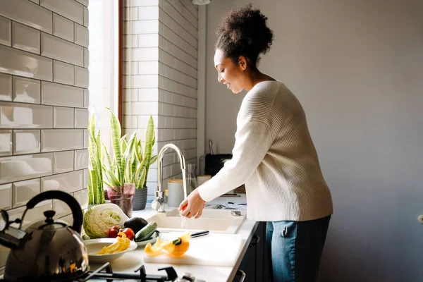 stock image Adult beautiful african pregnant woman washing vegetables to cook salad in cozy kitchen at home