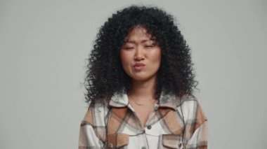 Displeased brunette Asian woman looking at the camera in the grey studio