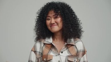 Cheerful brunette Asian woman waving hands at the camera in the grey studio