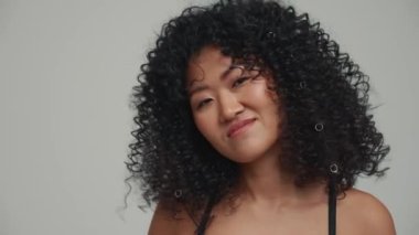 Portrait of cute brunette Asian woman dancing at the camera in the grey studio