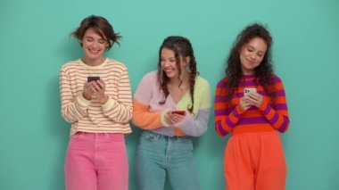 Three positive young girls typing on phones in the turquoise studio