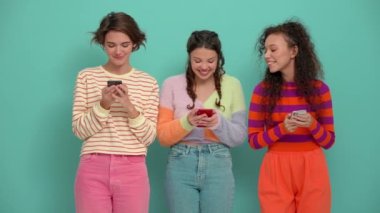 Three happy young girls typing on phones in the turquoise studio