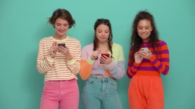 Three lovely young girls typing on phones in the turquoise studio