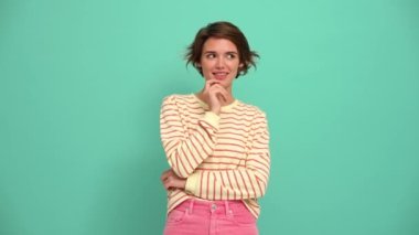 Cute young woman with short hairstyle showing silence gesture at the camera in the turquoise studio