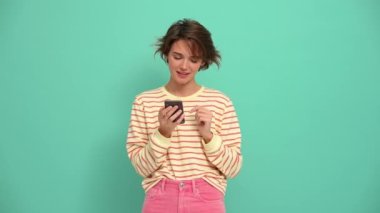 Handsome young woman with short hairstyle texting on phone in the turquoise studio