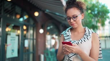 Gözlük takan güzel Afrikalı kadın dışarıda yürürken cep telefonunda yazı yazıyor.