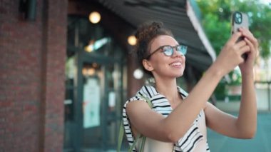 Gözlüklü Afrikalı pozitif bir turist açık havada caddenin fotoğraflarını çekiyor.