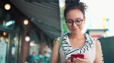 Dışarıda yürürken telefonda yazan gözlüklü, pozitif Afrikalı bir kadın.