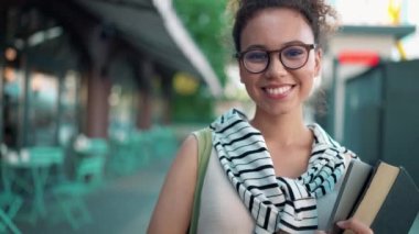 Elinde kitaplarla kameraya bakan gülümseyen Afrikalı kadın.