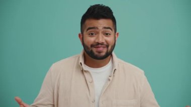 Heyecanlı Orta Doğulu genç adam turkuaz stüdyoda kamerayla konuşuyor.