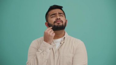 Ortadoğulu genç adam turkuaz stüdyoda bir şeyler düşünüyor.