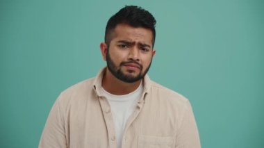 Konsantre Ortadoğulu genç adam kamerayla konuşuyor ve turkuaz stüdyoda bir şeye karşı çıkıyor.