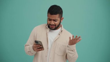 Şok olmuş Orta Doğulu genç adam turkuaz stüdyoda cep telefonuyla yazı yazıyor.