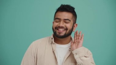 Pozitif Ortadoğulu genç adam sırları dinliyor ve turkuaz stüdyoda el hareketi yapıyor.