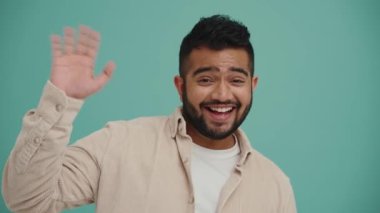 Orta Doğulu yakışıklı genç adam turkuaz stüdyoda kameraya selam veriyor.