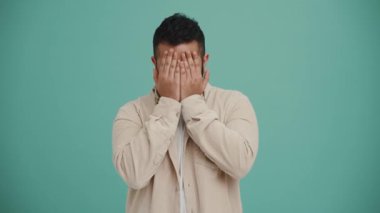 Turkuaz stüdyoda saklambaç oynayan komik Orta Doğulu genç adam.