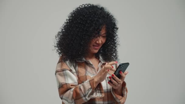 漂亮的黑发亚洲女人在灰色工作室用电话发短信 — 图库视频影像