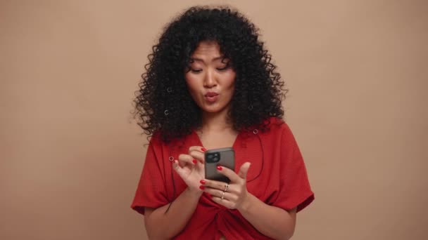 Confident Curly Haired Asian Woman Texting Mobile Beige Studio — Vídeo de Stock