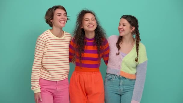 Три Позитивні Молоді Дівчата Обіймаються Дивляться Камеру Бірюзовій Студії — стокове відео