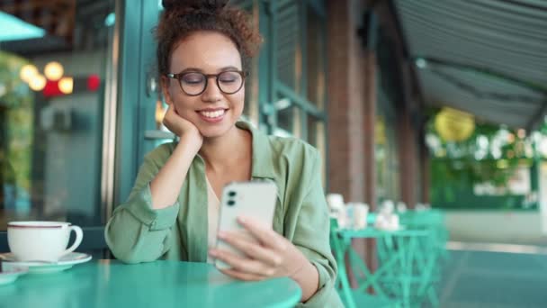 在户外咖啡馆里 穿着绿色衬衫和眼镜在手机上打字的非洲妇女得到了放松 — 图库视频影像