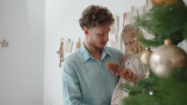 Drăguț Tată Fiică Discutând Conuri Lângă Pomul Crăciun Acasă — Videoclip de stoc
