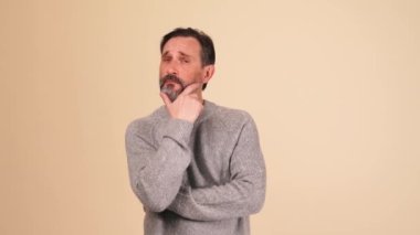 Gri kazak giyen kendine güvenen yetişkin sakallı adam bej renkli stüdyoda bir şeye katılıyor.